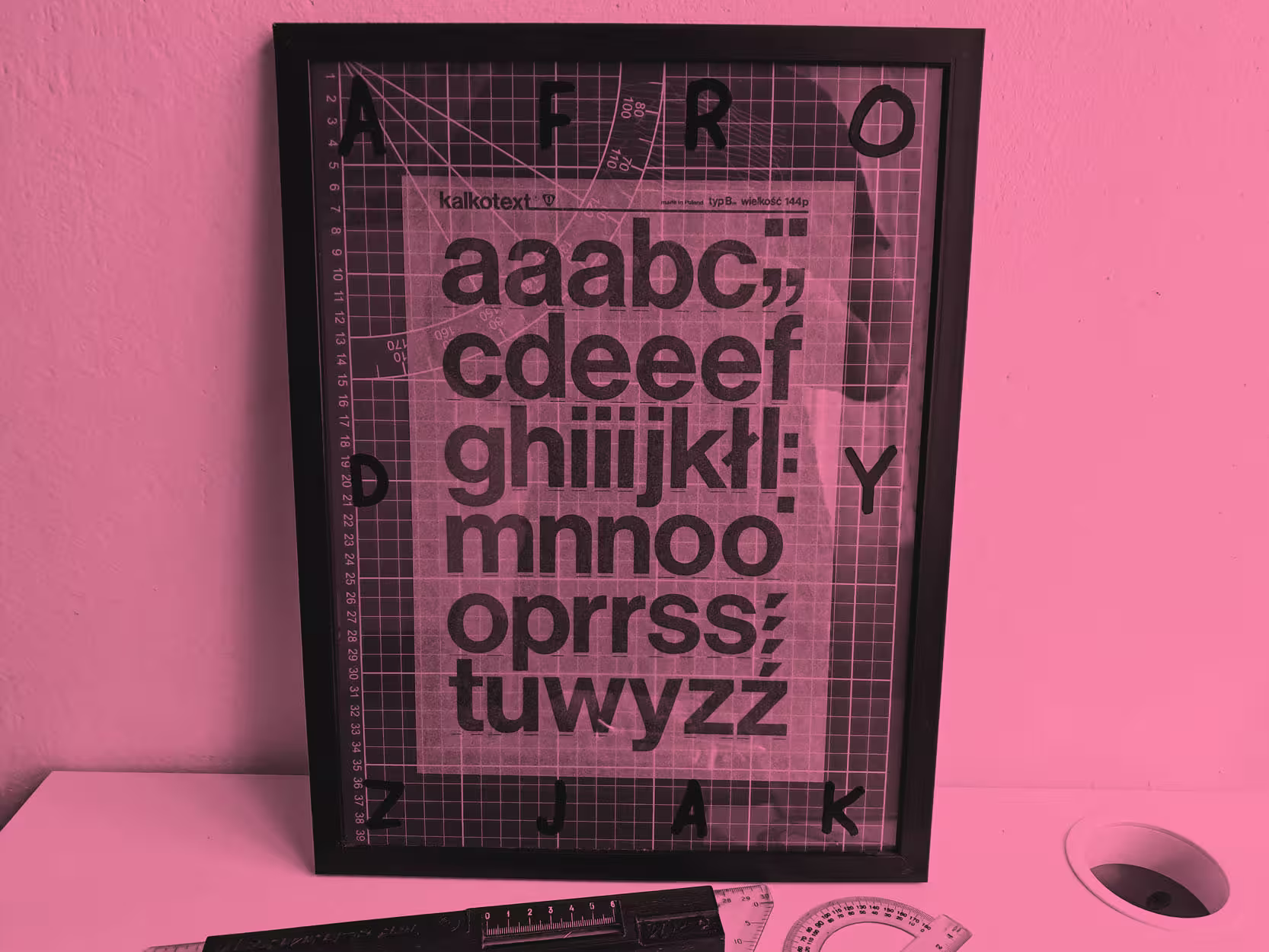 Obrazek w ramce który zawiera matę z centymetrową podziałką i arkusz Letrasetu z typografią