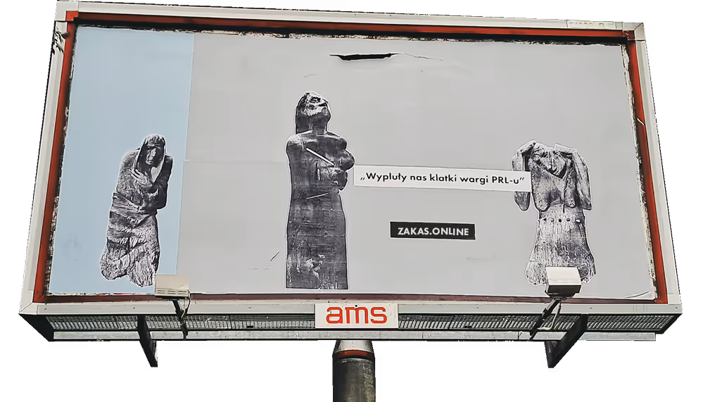 Zdjęcie billboardu ze sztuką uliczną. Naklejone są wielkie zdjęcia rzeźb z osiedla Kozanów i napis: wypluły nas klatki, wargi PRL-u